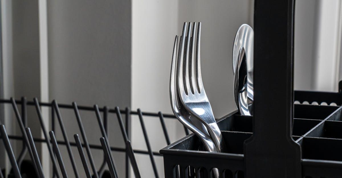 Close-up of stainless steel forks in a dishwasher rack, reflecting light and showcasing modern kitchenware.