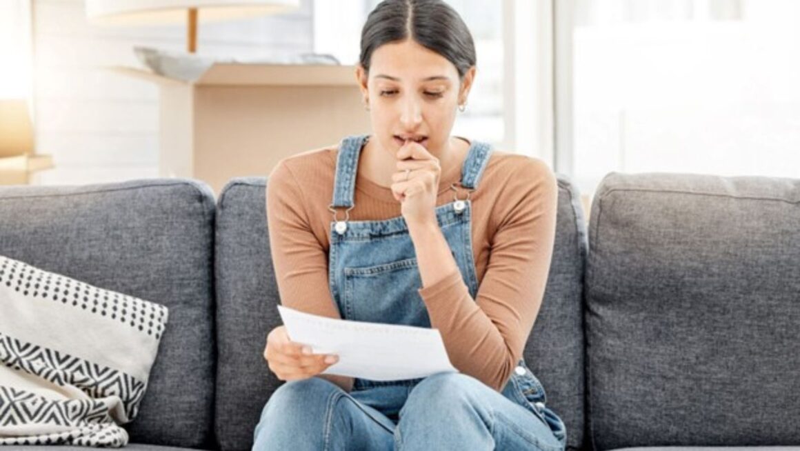 A young girl reading eviction record notice on couch.
